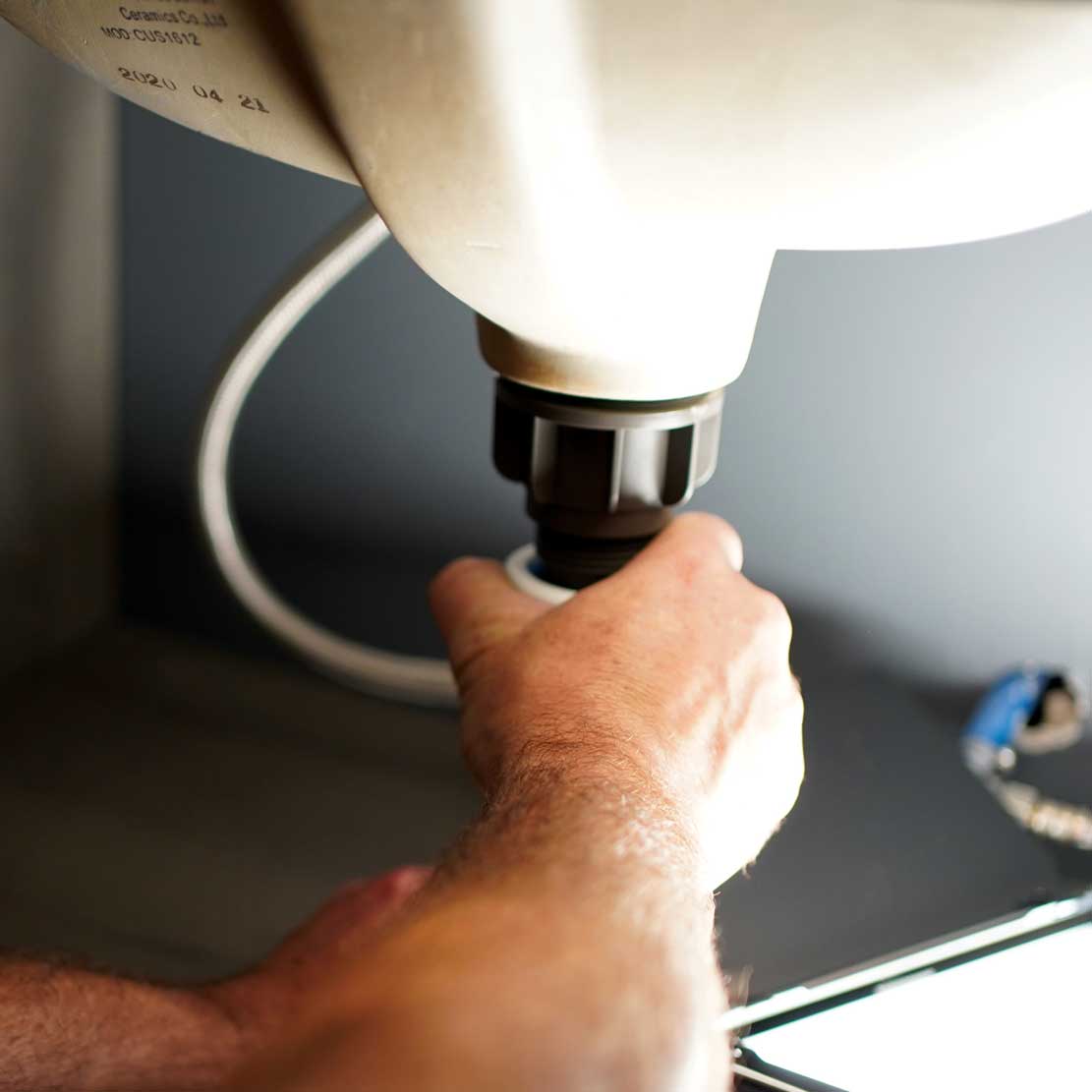 Plumber with plumbing equipment kneeling under a sink Fixing a sink